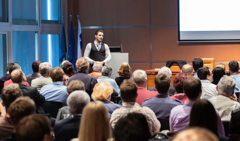 Speaker giving a talk in conference hall at business meeting event. Rear view of unrecognizable people in audience at the conference hall. Business and entrepreneurship concept.