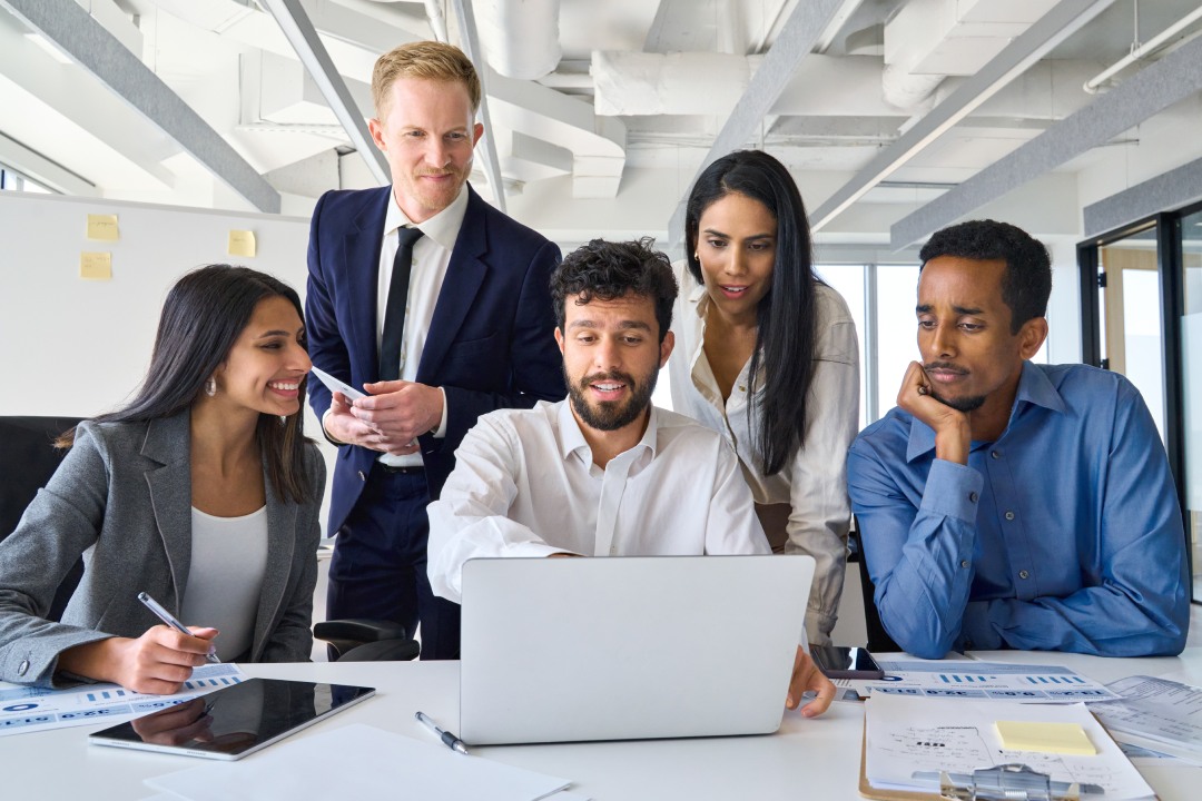 Busy diverse professional business people executives looking at laptop in office. International workers group and team leader having teamwork discussion managing project at work in meeting room.