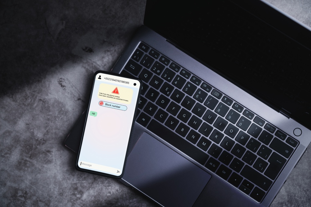 Smartphone laying on laptop receives message from suspected number scam. Unwanted anonymous call. Fraud and phishing phone concept. Message from stranger.
